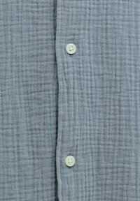 Υφασμα ανοιχτού γκρι με υφή, κάθετη ραφή και δύο λευκά κουμπιά τετράγωνα με τέσσερις τρύπες ραμμένα.