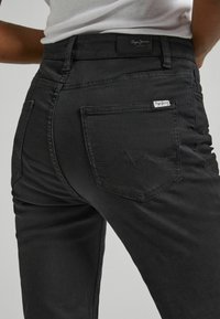 Melnas denim bikses ir ar pieguļošu dizainu, redzamām aizmugurējām kabatām ar kontrastējošām šuvēm un zīmola etiķeti uz jostasvietas.