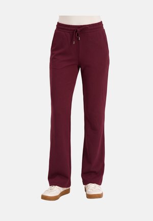 Maroonkleurige joggingbroek met elastische taille en trekkoord, rechte pijpen, gedragen met witte sneakers op een persoon tegen een effen achtergrond.