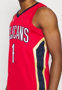 Red basketball jersey featuring "PELICANS" text, number "1," and side stripes in navy blue and gold. Made from breathable fabric.