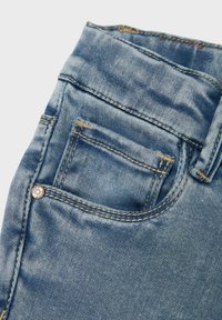 Des jeans en denim bleu clair présentent un design classique avec une poche avant, des coutures visibles et un accent en bouton métallique près de la taille.