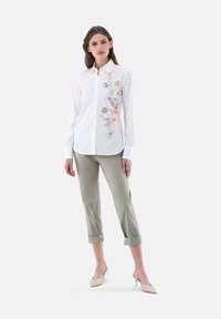 White button-up shirt with floral embroidery in pastel colors on one side, paired with light green cropped pants and beige heels.