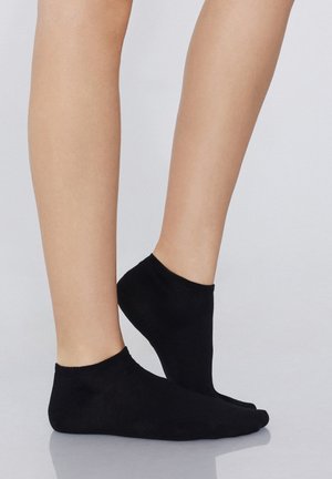 Schwarze Knöchelsocken aus weichem, dehnbarem Material, mit einer glatten Textur und ohne sichtbare Muster, die auf nackten Füßen liegen.