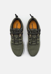 Zielone tekstylne sneakersy z czarnymi sznurowadłami, białą podeszwą i kontrastującą pomarańczową wkładką. Posiadają logo na języku oraz teksturowaną cholewkę.