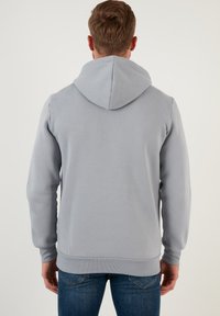 Sudadera gris con capucha, con mangas largas, puños elásticos y cintura elástica, hecha de tela suave, mostrada desde atrás.