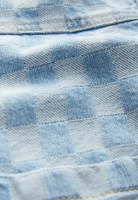 Tissu en denim bleu clair avec un motif à carreaux, doté d'une surface texturée et de coutures contrastantes. La vue en gros plan met en évidence les détails.