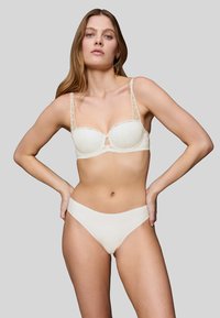 Slonovinový podprsenka s průhlednými krajkovými ramínky, tvarovanými košíčky a centrálním výřezem. Ladící bezešvé vysoké kalhotky v hladké matné úpravě.