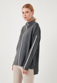 Grey knit sweater with a high collar, white side stripes, and side slits. Features a relaxed fit and soft texture.