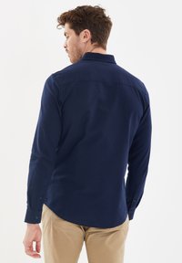 Marineblauw overhemd met lange mouwen, standaardkraag, knoopsluiting bij de manchetten en een gladde textuur, met een gebogen zoomlijn.