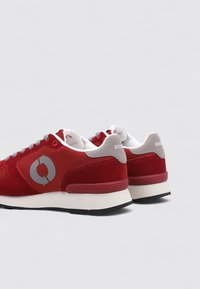 Zapatillas de ante rojo con detalles y logo en gris. Cuentan con una media suela blanca y una suela exterior de goma negra. Cordones con ojales y collar acolchado.