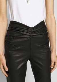 Pantaloni in ecopelle neri con texture arricciata in vita, abbinati a una maglietta bianca con un design a righe verdi.