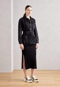 Svart denimjakke med belted liv, to frontlommer; kombinert med en svart ribbet midi-skjørt med siden splitt og klumpete joggesko.