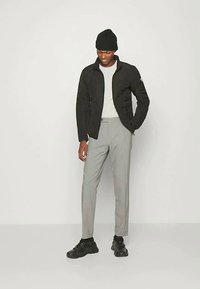 Svart quiltet jakke med ståkrage, lys grå t-skjorte, grå bukser og svarte joggesko. Modell med svart lue.