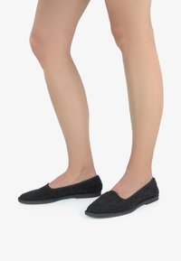 Mustad mustad kingad, millel on tekstuuriga, karvane ülemine osa ja lame kummist tald. Disain on minimalistlik koos ümarate varvastega.