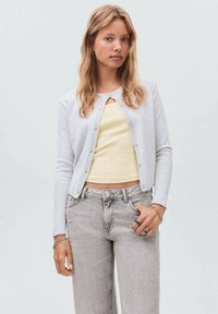 Lichtgrijze cardigan met een ronde hals en knoopsluiting, gedragen over een lichtgele top en gecombineerd met vervaagde grijze jeans.