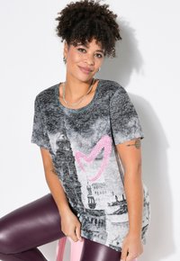 Camiseta gris de manga corta con estampado de paisaje urbano y un diseño de corazón de strass rosa. El tejido es suave, con un corte relajado y cuello redondo.