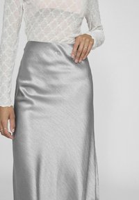 Jupe en satin argenté avec une texture lisse et un design élégant et ajusté. Une main délicate repose à côté de la jupe.