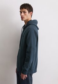 Hoodie bleu foncé en tissu mélangé avec une poche kangourou, capuche à cordon de serrage et poignets côtelés. Tissu en coton doux, coupe décontractée, détail minimal de logo.