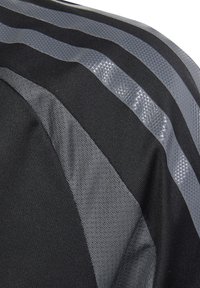 Schwarzer und grauer Stoff mit einer Mischung aus glatten und strukturierten Oberflächen, diagonalen Streifen und einem geometrischen Muster auf einem transparenten Abschnitt.