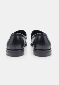 Zapatos de cuero negros con una textura suave, puntera redondeada, diseño de perfil bajo y suelas de cuero marrón en contraste.
