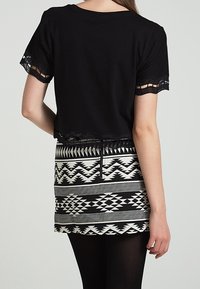 Top nero corto con maniche corte caratterizzato da dettagli in pizzo testurizzato e una gonna bianca con motivo geometrico in bianco e nero.