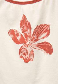Hvidt stof med et centralt koralblomstprint, der har brede kronblade og detaljeret tekstur, kantet af en kravekant i koralfarve.