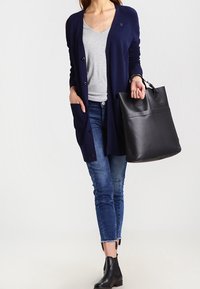 Námořnický dlouhý cardigan s žebrovanými rameny, šedé tričko, skinny džíny a černá kabelka. Obsahuje džíny po kotníky a černé kotníkové boty.