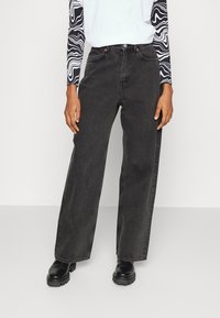 Jeans de pierna ancha negros hechos de denim, con una cintura alta, dos bolsillos frontales y un corte recto. Combinados con una blusa de manga larga con estampado.