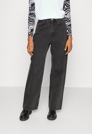 Jeans de pierna ancha negros hechos de denim, con una cintura alta, dos bolsillos frontales y un corte recto. Combinados con una blusa de manga larga con estampado.