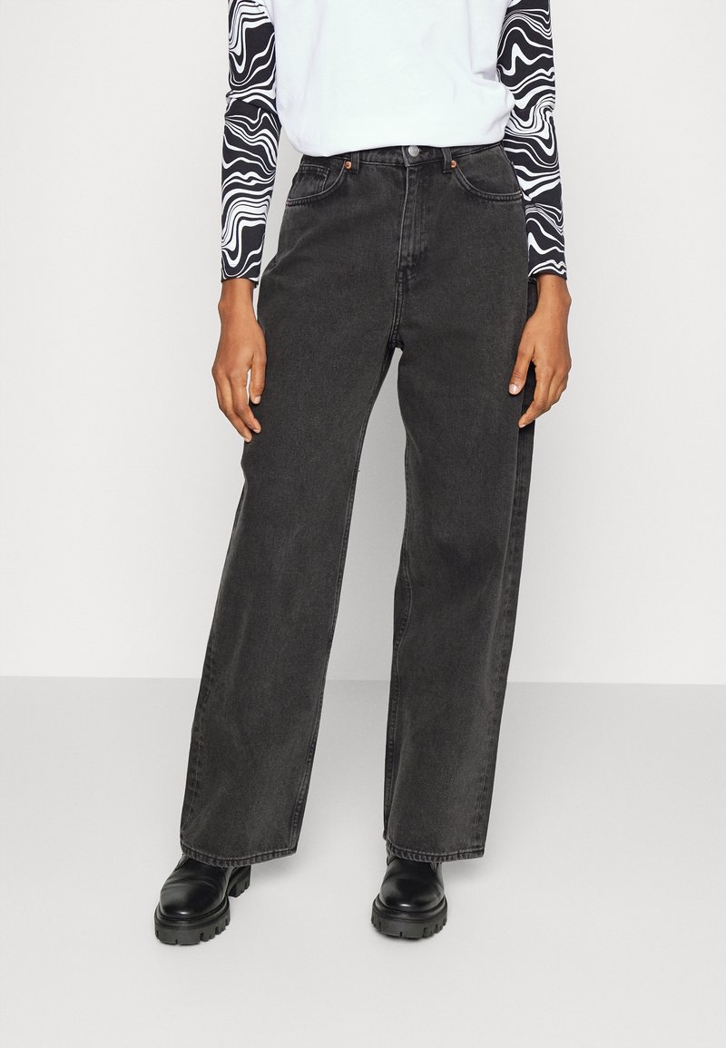 Jeans de pierna ancha negros hechos de denim, con una cintura alta, dos bolsillos frontales y un corte recto. Combinados con una blusa de manga larga con estampado.