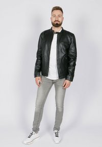 Chaqueta de cuero negra con cuello elevado, frontal con cremallera y bolsillos laterales; combinada con una camisa blanca, vaqueros grises y deportivas blancas.