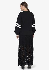 Sweatshirt noir surdimensionné avec des accents de rayures blanches et de longues manches bouffantes, associé à une jupe maxi noire en dentelle ornée d'un motif floral.