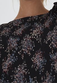 Fladdrande svart plisserad tyg med ett blommönster i dämpat röd, blå och vit. Urringningen har en rynkad design och en texturerad yta.