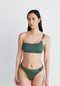 Σέτ πράσινου μπικίνι με έναν ώμο, ενσωματωμένο μεταλλικό στοιχείο και κόμπους στα πλάγια του κάτω μέρους, φτιαγμένο από λεία, ελαστική ύφανση.