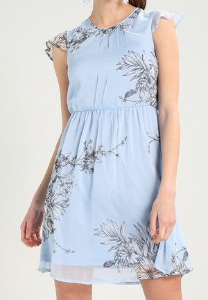 Light blue sleeveless dress with black and white floral prints, gathered waist, and flutter sleeves worn by a person standing.