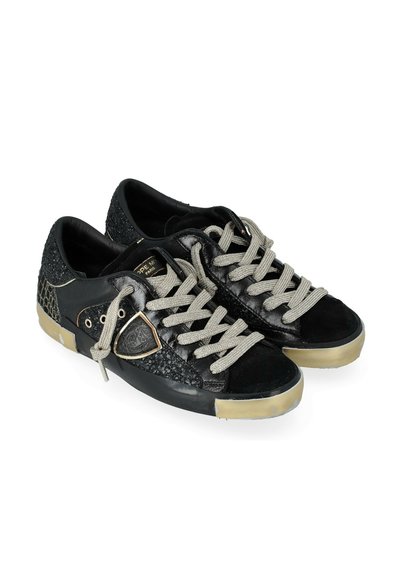 Sneaker nere basse con lacci grigi, pannelli laterali testurizzati, suole beige usurate e un piccolo logo a forma di scudo sul lato esterno.
