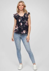 Blouse noire à fleurs avec des manches volantes, ornée de motifs rose clair et verts. Associée à un jean skinny bleu et des baskets blanches.