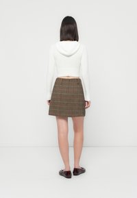 Cropped white hoodie with a hood, paired with a brown checkered skirt featuring red accents, and brown shoes. Back view displayed.