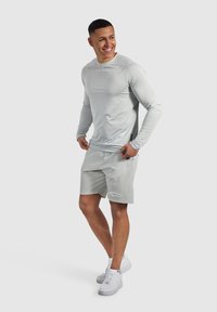 Helles graues, athletisches Langarmhemd und passende Shorts. Mit feuchtigkeitsableitendem Gewebe, ergonomischen Nähten und reflektierenden Akzenten.
