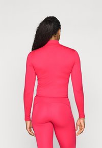Elegante lyse pink langærmet top med høj krave, glat tekstur og sømløst design, parret med matchende leggings. Set bagfra.