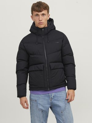 Black puffer jacket with a hood, featuring a front zipper, two large pockets, and elastic cuffs. Worn over a purple shirt and blue jeans.