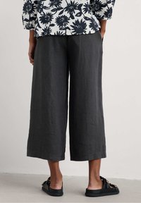 Grijze wijde linnen broek met een textuurafwerking, voorzien van zijzakken en een relaxte pasvorm, gecombineerd met zwarte sandalen.