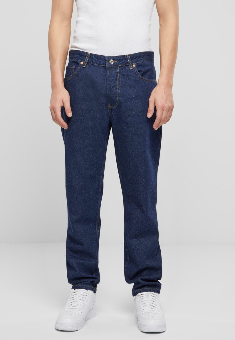 Jeans de mezclilla azul oscuro con un corte recto, cinco bolsillos y costuras claras. La parte delantera cuenta con un cierre de botón y cremallera.