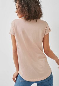 Lichtroze t-shirt met opgerolde korte mouwen, ronde zoom en een zachte textuur. Gestyled met een blauwe jeans, gezien vanaf de achterkant.