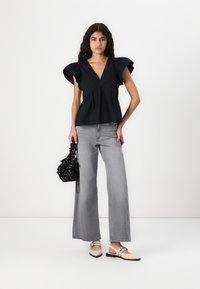 Svart bomullströja med V-ringning och utsvängda ärmar, matchad med grå vida jeans. Accessoarer inkluderar en mönstrad svart väska och nude klackar.