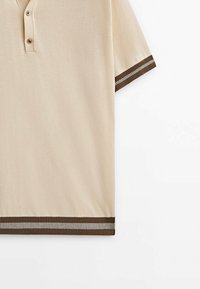 Polo beige à manches courtes avec deux boutons, avec bordure côtelée marron et grise aux poignets des manches et à l'ourlet.