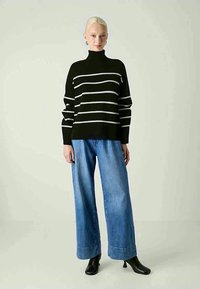 Schwarz gestreifter Rollkragenpullover mit weißen horizontalen Streifen, kombiniert mit weit geschnittenen blauen Jeans und schwarzen Stiefeletten. Glatte Textur über das gesamte Material.