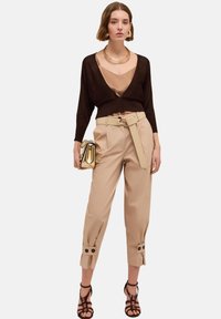 Brun cardigan över en beige camisole, kombinerad med beiga högmidjade byxor med bälte och knappdetaljer. Accessoarer med en guldfärgad väska.