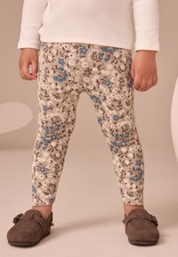 Leggings a coste in bianco sporco con motivo floreale in blu e marrone. Abbinati a mocassini in camoscio marrone con dettagli decorativi.