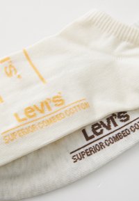 Levi's medvilninės kojinės kremų spalvos, su geltona ir ruda atspausdinta tekstu. Minkšta tekstūra su išlygintais kraštais ir logotipo detalėmis.